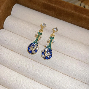 Détail de boucles d'oreilles luth dorées avec émail bleu-vert, perles et strass