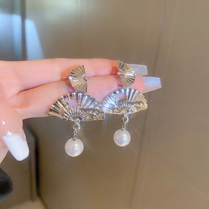 Détail de la boucle d'oreille éventail argentée avec motif ciselé et perle blanche