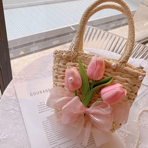 Close-up of handmade straw bag with pink tulips, white pearls and a large soft bow