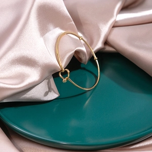 Detailed view of a gold knot bracelet with heart-shaped cutout on luxury silk background