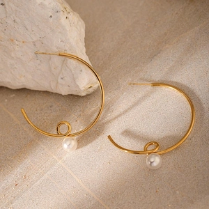 Close-up of golden C-shaped twisted earring with a white pearl on a stone background