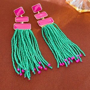 Macro shot of long fringe earrings featuring pink enamel cubes and green beaded tassels