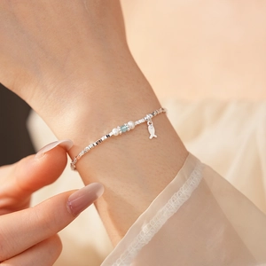 Macro shot of silver pearl bracelet with blue gemstone and small fish charm on wrist