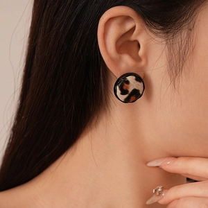 Detail of round leopard print earring with fabric texture and black border on a model