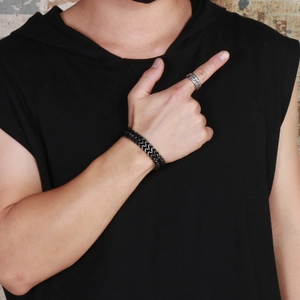 Detail of model wearing a black woven dragon scale bracelet and silver ring on a brick wall