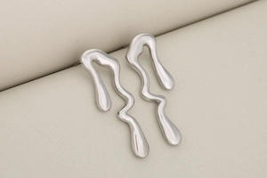 Détail macro de boucles d'oreilles en métal liquide argenté au design lave irrégulier