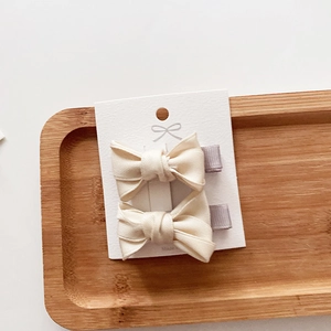 Detailed view of two cream white fabric bow hair clips on a wooden tray background