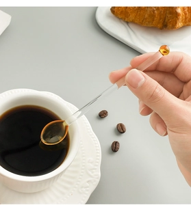 Close-up of a hand using a long-handle heart glass spoon to stir coffee in a white cup