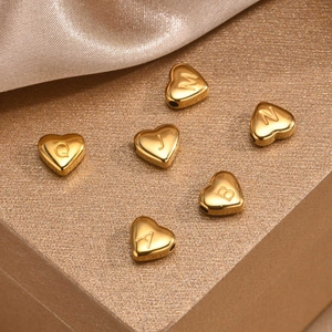 Macro detail of gold heart-shaped alphabet beads on champagne silk fabric background