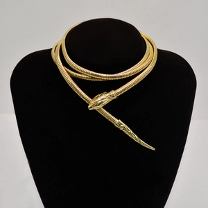 Detailed view of a gold snake-shaped metal necklace with intricate carvings on a mannequin
