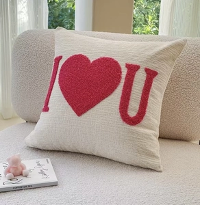 Close-up of beige cushion cover with red textured heart embroidery on soft sofa