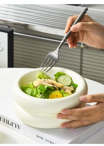 Close-up of hand using a silver fork to eat salad from a creamy white ceramic donut bowl