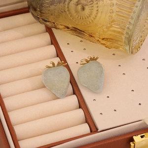 Cute light green strawberry stud earrings with gold leaves on a brown leather jewelry box