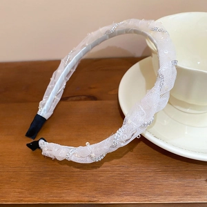 Close-up of white lace headband with elegant pearls and sparkling rhinestone chains