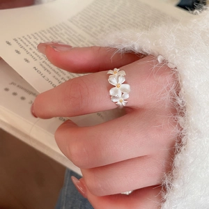 Detailed close-up of a silver flower ring with white petals and yellow centers on a finger