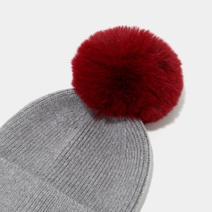 Detailed shot of dark grey ribbed knit hat featuring a fluffy burgundy faux fur pom-pom