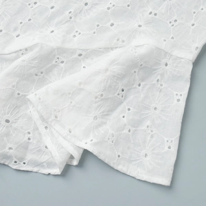 Detailed close-up of intricate sunburst broderie anglaise embroidery on white cotton fabric