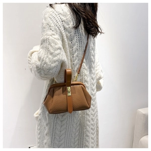 Brown lychee texture leather handbag with gold buckles worn over white knit cardigan