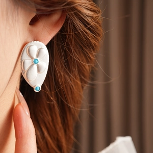 Macro shot of silver teardrop earring with flower relief and blue turquoise stones