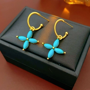 Detail of twisted gold hoop earrings with turquoise clover pendants on black jewelry box