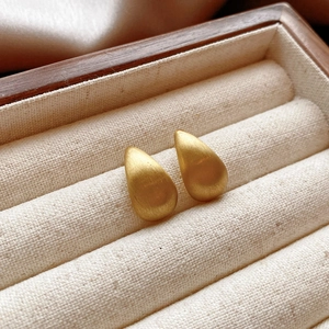 Detail of matte brushed gold water drop earrings on premium beige linen background
