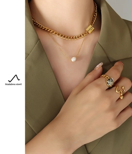 Detail of layered gold stainless steel necklace with pearl and engraved rectangular charm