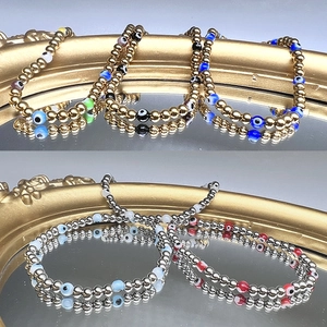 Detailed view of 18K gold and silver beaded bracelets with colorful evil eye charms