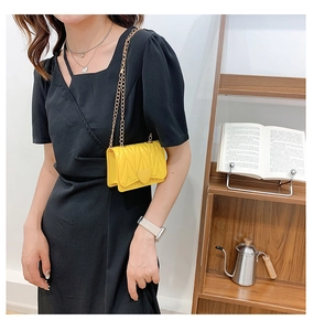 Detail of yellow heart-shaped mini crossbody bag with gold chain strap on model