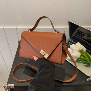 Brown embossed leather handbag with metal twist lock held in a natural office setting