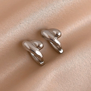 Macro shot of polished silver twist huggie earrings on premium champagne silk fabric