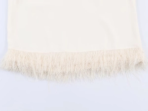 Detailed macro view of the beige top featuring dense fringe and feather trim at the hemline