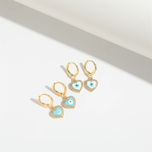Macro shot of gold heart dangle earrings with blue evil eye motifs and zircon pavé