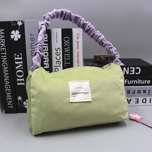 Detail of light green corduroy handbag with contrasting purple scrunchie handle and label