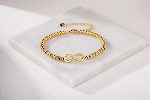 Detailed close-up of golden infinity symbol bracelet with beaded chain on marble tray