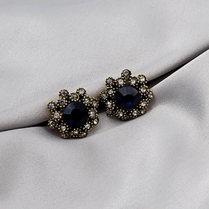 Macro detail of vintage gold flower stud earrings with deep blue gemstones and white crystals