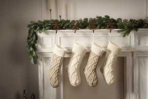 Detail of four knit Christmas stockings in cream and oatmeal hanging on a white fireplace