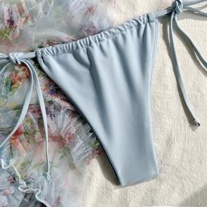 Detail of light blue tie-side bikini bottom with floral mesh cover-up on beige fabric