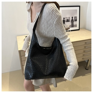 Detailed view of black woven leather tote bag texture on a shoulder-carried model