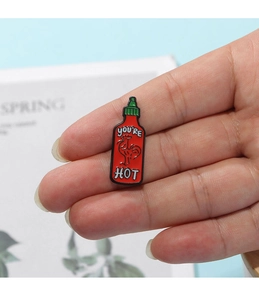 Detail of creative hot sauce enamel pin with You're Hot text on a hand-held backpack badge