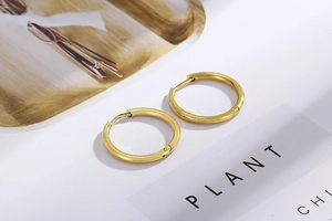 Close-up of golden hoop earrings with a secure hinged closure on a minimalist background