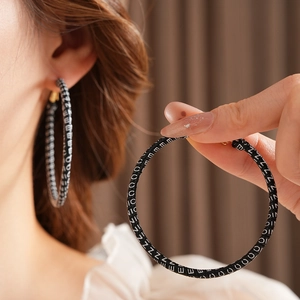 Detailed view of large black leather hoop earrings with white repeated NICE text pattern