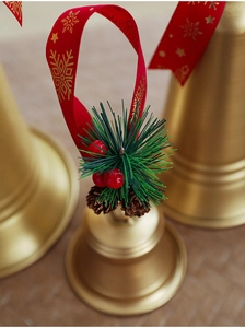 Macro shot of gold Christmas bell with red snowflake ribbon and pine cone accents