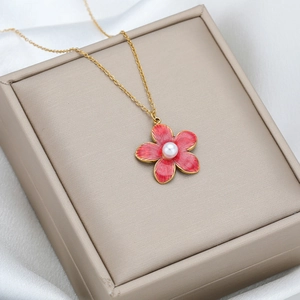 Golden necklace with red enamel flower and pearl pendant on a beige gift box