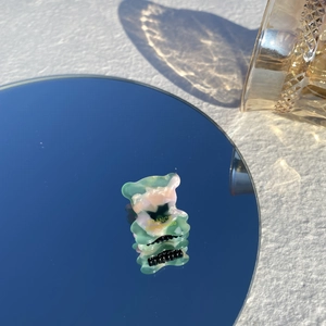 Détail d'une mini pince à cheveux ours en acétate marbré vert sur une surface miroir