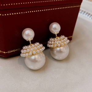 Vue macro de boucles d'oreilles perles double-face avec détails dorés sur boîte à bijoux