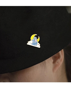 Detailed shot of an enamel rabbit brooch on a yellow moon and white cloud on a black hat