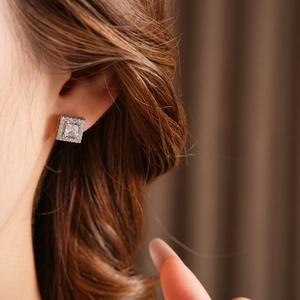 Close-up of elegant square zircon earrings worn on ear showing sparkling silver details