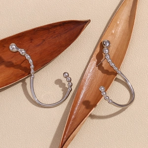 Macro detail of silver irregular beaded J-shape earrings on natural dried leaves