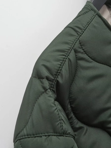 Detail of dark green quilted jacket featuring diamond stitching and round neckline