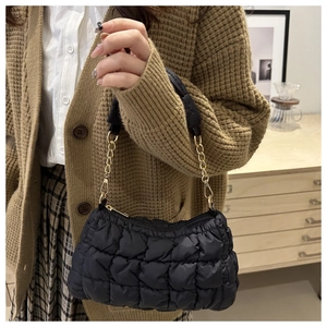 Détail du sac matelassé noir avec chaîne dorée porté par un mannequin en intérieur